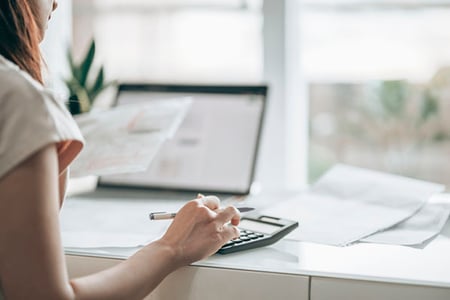 Frau berechnet Preis-Absatz-Funktion mit Taschenrechner und Laptop